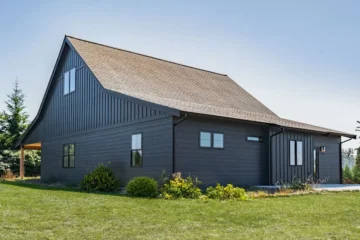 Rear exterior of a converted garage with residential loft and ground floor addition. Some bushes and flowers as landscaping.